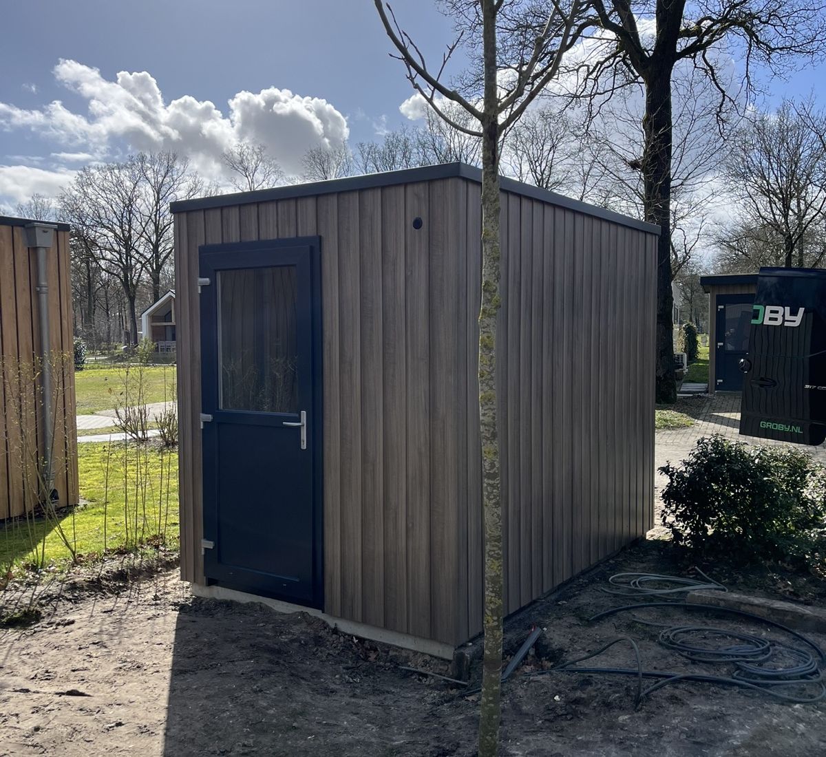 voorkant maatwerk berging houtcomposiet met Groby bus op achtergrond